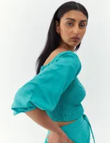 Top corto de color turquesa con cuerpo fruncido tipo nido de abeja, escote cuadrado y mangas abullonadas.