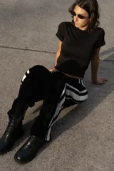 Pantalón negro de terciopelo con corte holgado y cintura elástica. Presenta dos líneas blancas verticales a los costados y la palabra "LESS" bordada en el muslo izquierdo.