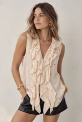 Blusa sin mangas de color beige, con escote en V pronunciado y grandes volados frontales. Presenta pequeños detalles bordados en toda la prenda.
