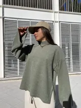 Poleron de tejido suave color verde, con cuello alto, corte holgado y mangas amplias con aberturas laterales en el ruedo.