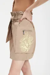 Minifalda color tostado de tejido tecnológico con cierre frontal con cremallera metálica, bolsillos laterales con fuelle y lazo en la cintura.