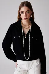 Saco negro de tejido de punto en mezcla de baby alpaca y lana, con cuello camisero, cierre frontal con cremallera con dije de perla, bolsillos frontales con solapa y botones decorativos.