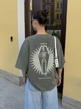 Remera oversize de color marrón topo con efecto acid wash, cuello redondo y manga corta. Cuenta con un pequeño estampado gráfico frontal con el texto 'WAKE UP IND' y una calavera.
