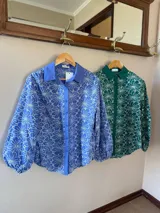 Camisa de manga larga con diseño de flores bordadas en color blanco sobre base azul. Presenta cuello clásico, cierre frontal con botones y mangas abullonadas con puños elásticos.