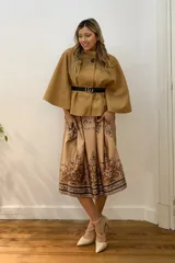 Capa corta negra de paño italiano con cuello alto y cinturón con hebilla dorada.