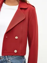 Chaqueta corta tipo blazer en color bordó, con diseño de doble botonadura frontal, solapas clásicas y detalles de charreteras en los hombros con botones metálicos.