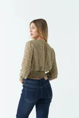 Blusa de manga larga con estampado floral pequeño sobre fondo oscuro. Presenta escote en V con lazo para anudar, cintura con frunce elástico y puños ajustados.
