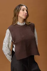 Chaleco de punto color marrón, con cuello redondo y corte recto. Presenta un diseño minimalista con aberturas laterales amplias y detalle de tira con botón en los costados.