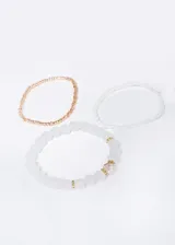 Set de tres pulseras elásticas con cuentas de plástico: una dorada, una blanca y una con cuentas blancas más grandes con detalles dorados y una cuenta facetada rosada.