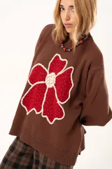 Buzo de punto color chocolate con diseño de flor grande en el frente en tonos rojos y centro texturizado en color crema. Presenta cuello redondo, mangas largas y puños y ruedo acanalados.