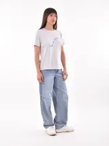 Remera blanca de manga corta con estampado frontal que dice "hecha pa brillar" en tonos rosados y estrellas.