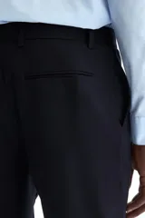 Pantalón de traje negro de corte slim fit, con bolsillos laterales, bolsillos traseros ribeteados y raya marcada en las perneras. Cuenta con cierre de cremallera y corchete oculto.
