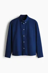 Camisa de manga larga H&M de corte relajado, confeccionada en algodón Oxford azul marino. Cuenta con cuello americano, bolsillo aplicado en el pecho y botones frontales blancos.