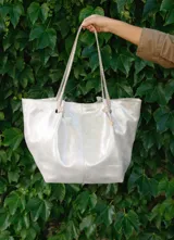 Bolso tipo tote de cuero color plateado con acabado metalizado. Tiene doble asa de hombro con detalle de nudo.