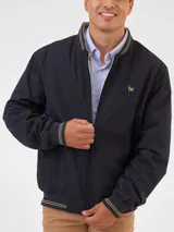 Campera bomber reversible azul marino y beige con cuello, puños y ruedo acanalados con rayas doradas. Tiene cierre frontal y logo bordado en el pecho.