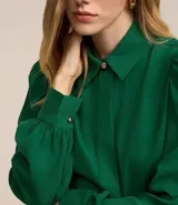 Camisa celeste de crepé con cuello inglés, manga larga abullonada y abotonadura frontal.