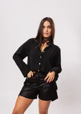 Camisa negra de cuello redondo con frunces y mangas largas con puños abiertos.
