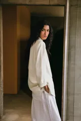 Blazer blanco de lino con cuello solapa, manga larga con hombreras y puños con vuelta estampada. Tiene bolsillos delanteros con solapa y cierre frontal con botón.