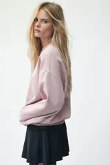 Buzo de tejido de punto color rosado pálido, con cuello redondo, hombros caídos y puños y bajo acanalados. Presenta un estampado frontal en blanco con el texto "Firenze Italia" y un escudo central con el año "1932".