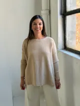 Sweater de punto en color beige, con cuello redondo, mangas largas con puños ajustados y diseño holgado con aberturas laterales en el ruedo.