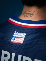 Camiseta de fútbol Umbro del Club Nacional de Football, modelo Away 2. Diseño azul con detalles en blanco y rojo en cuello y mangas. Incluye logo de Umbro, escudo del club y sponsor Antel en el frente.