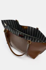Bolso tipo shopper de color marrón, con diseño minimalista, doble asa de hombro y cierre magnético. Incluye un colgante decorativo con detalle de cinta en tonos claros y un bolsillo interior amplio.