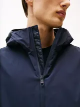 Campera azul marino con capucha, cierre de cremallera, dos bolsillos en la cintura y puños elásticos con botones a presión. Tiene un parche con el logo de Tommy Hilfiger en la manga.