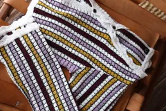 Blusa de tejido de punto calado a rayas horizontales en tonos borgoña, amarillo, lila y blanco. Tiene mangas largas que se ajustan en el codo y se ensanchan hacia el puño.