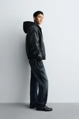 Cazadora estilo bomber de corte relajado confeccionada en tejido efecto piel color negro. Presenta capucha integrada, cierre frontal de cremallera, bolsillos laterales de vivo y puños y bajo con acabado en rib. El interior cuenta con forro acolchado en color naranja.