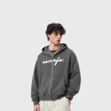 Buzo con cierre frontal tipo hoodie, color gris oscuro con efecto lavado. Presenta un estampado con tipografía cursiva en el pecho y bolsillos tipo canguro.