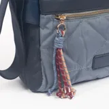 Bandolera de diseño bicolor en tonos azul y gris, con cuerpo acolchado en forma de rombos. Incluye cierre frontal con cremallera dorada, detalle de borla decorativa con cordones trenzados y correa ajustable para el hombro.
