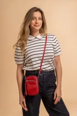 Bandolera porta celular color negro, confeccionada en símil cuero con textura granulada. Presenta un compartimento principal con cierre, un bolsillo frontal con cierre y detalle de borla decorativa, y correa regulable y desmontable.