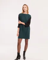 Vestido corto verde oscuro con mangas 3/4 negras, cuello bote y bolsillos laterales.