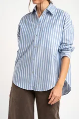 Camisa de algodón con rayas verticales celestes y blancas, de corte oversize, cuello camisero, manga larga y bolsillo aplicado en el pecho.