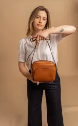 Bandolera de diseño compacto en color beige, confeccionada en material símil cuero con textura granulada. Cuenta con un bolsillo frontal con cierre y correa larga regulable.