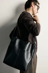 Bolso tipo shopper de diseño minimalista en color negro, con dos bolsillos planos exteriores y compartimento principal con cierre magnético. Incluye un bolsillo interior y asa de hombro ajustable.