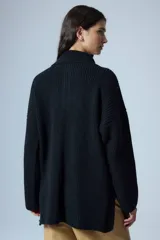 Sweater negro de cuello polo tejido con cierre diente de perro a tono y tajos laterales. Tiene un parche bordado con elementos del drop.