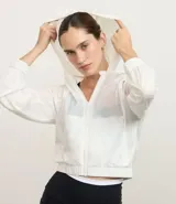 Campera rompevientos deportiva cropped de color blanco, con capucha, cierre frontal y puños elásticos. Confeccionada en poliamida, presenta un diseño ligero y funcional.