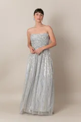 Vestido largo de tul bordado color gris claro, con lentejuelas plateadas y doradas. Modelo strapless drapeado y falda con movimiento.