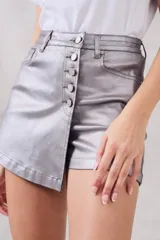 Skort plateada metalizada con cierre de botones frontal y corte asimétrico.