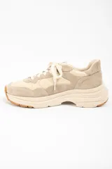 Zapatilla urbana de diseño chunky, confeccionada en una combinación de cuero liso y gamuza en tonos beige y arena. Presenta cordones al tono, suela de plataforma con relieve y detalle de marca grabado en el talón.
