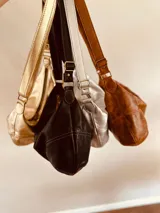 Cartera tipo banana bag de cuero color marrón oscuro, con correa ajustable para usar al hombro o cruzada.