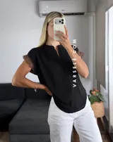 Blusa negra de tela Cey, con cuello mao y escote en V con cierre. Mangas cortas con detalle de encaje marrón en los hombros.