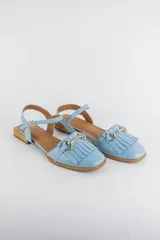 Sandalias de cuero color celeste, con punta cerrada, flecos frontales y detalle de estribo metálico dorado. Tienen tira ajustable al tobillo y suela plana con pequeño taco.