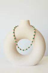 Collar tipo choker con diseño de cuentas esféricas verdes y cuentas cilíndricas con patrón de rayas rojas y blancas. Incluye cadena de extensión para ajuste.