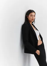 Blazer negro entallado de punto roma con solapas de muesca, hombros estructurados, abertura posterior y dos bolsillos de ribete delanteros.