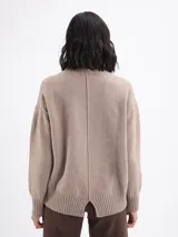 Buzo de punto color beige, con cuello alto y mangas largas con puños acanalados.