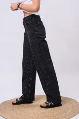 Pantalón wide leg de tiro alto confeccionado en denim negro, adornado con brillos de strass distribuidos por todo el frente.