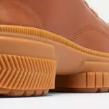 Bota de caña media Sorel, confeccionada en cuero impermeable color marrón tostado. Presenta un diseño moderno con cordones frontales, herrajes metálicos en forma de D y una suela de caucho robusta con plataforma dentada. Incluye tirador en el talón y cierre lateral para mayor practicidad.