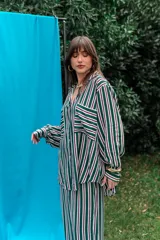 Conjunto de camisa y pantalón de fibrana con diseño a rayas verticales en tonos verde, blanco, violeta y negro. La camisa es de corte amplio con bolsillos frontales en el pecho, y el pantalón es de corte recto y holgado.